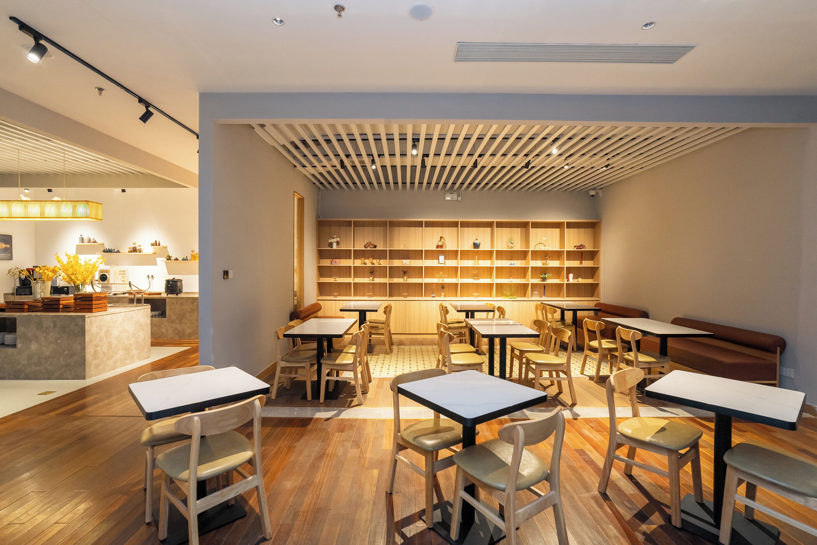 Et moderne restaurantmiljø med træborde og stole, en central disk og en reol med udstillingsobjekter.