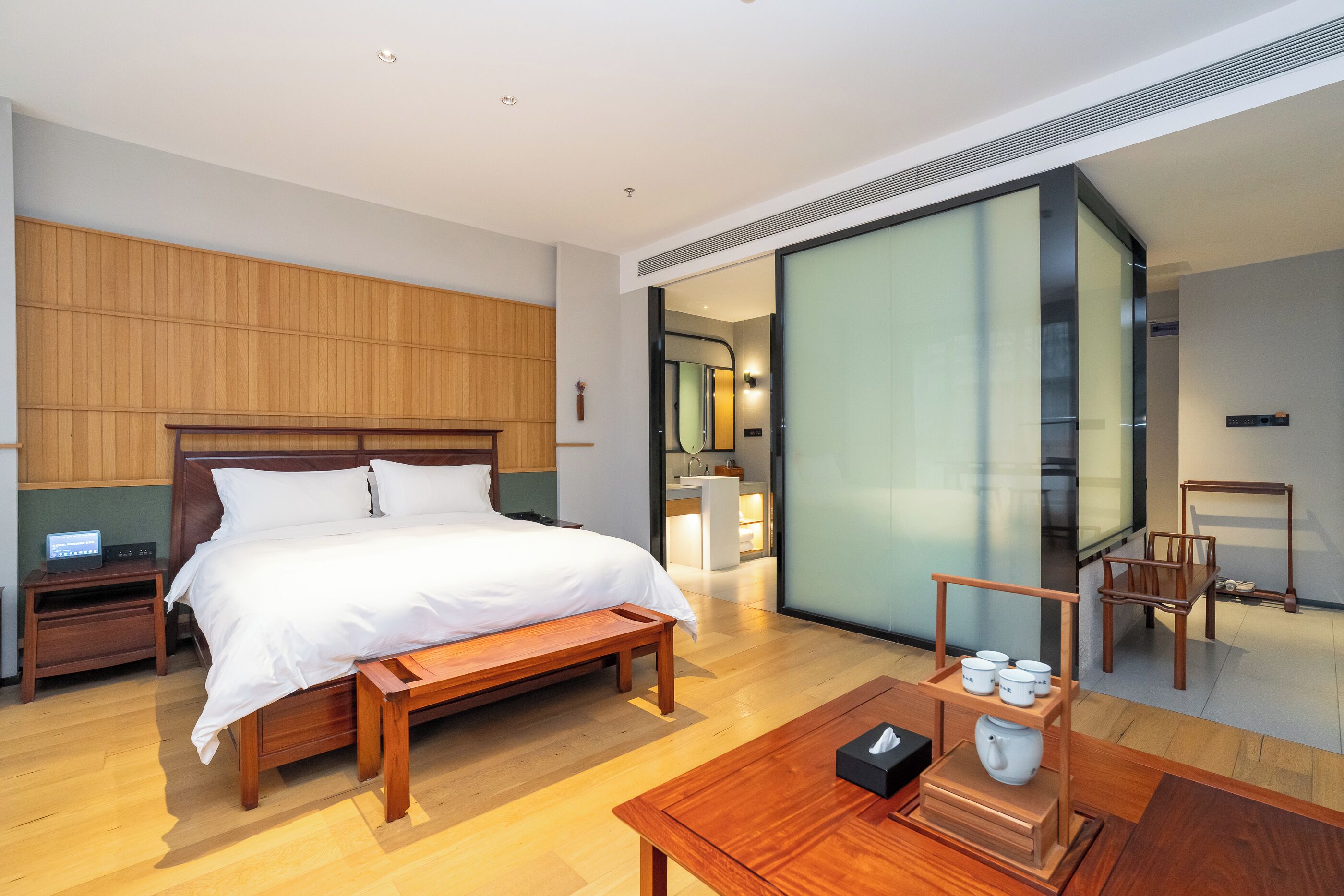 Een moderne hotelkamer met een houten bed, nachtkastjes, een houten salontafel en een schuifdeur naar een badkamer.