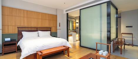 Een moderne hotelkamer met een houten bed, nachtkastjes, een houten salontafel en een schuifdeur naar een badkamer.