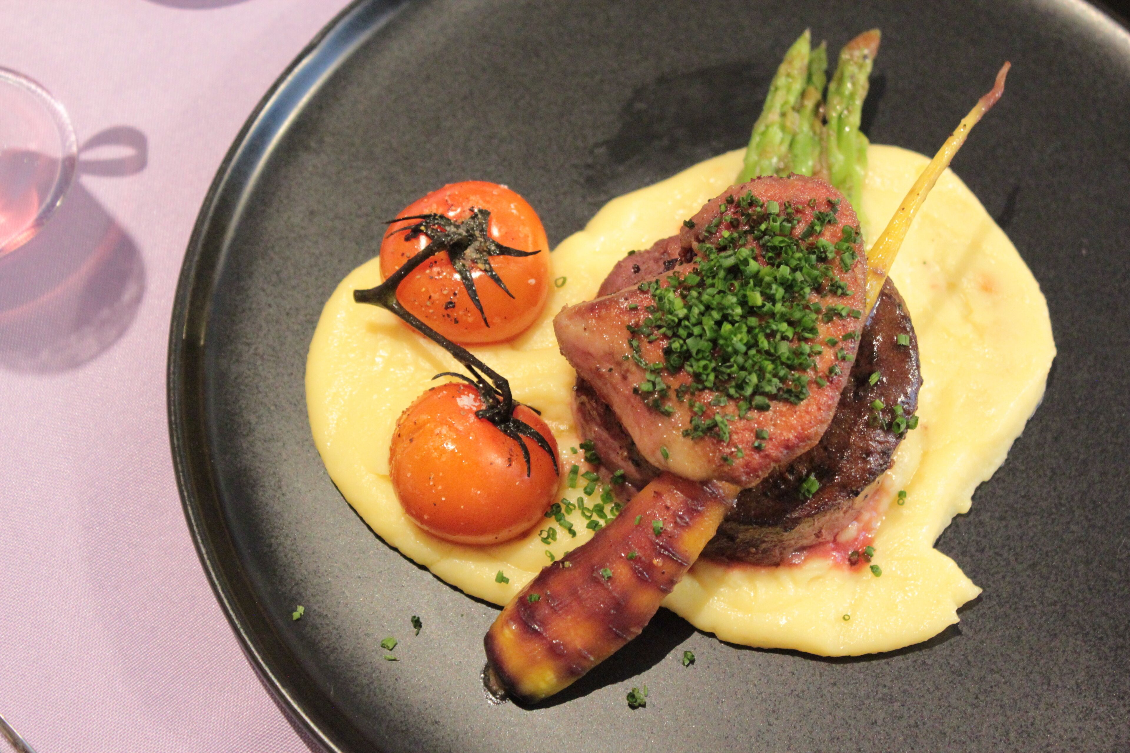 Ein Teller Essen mit Tomate, Spargel und einem Fleischstück.