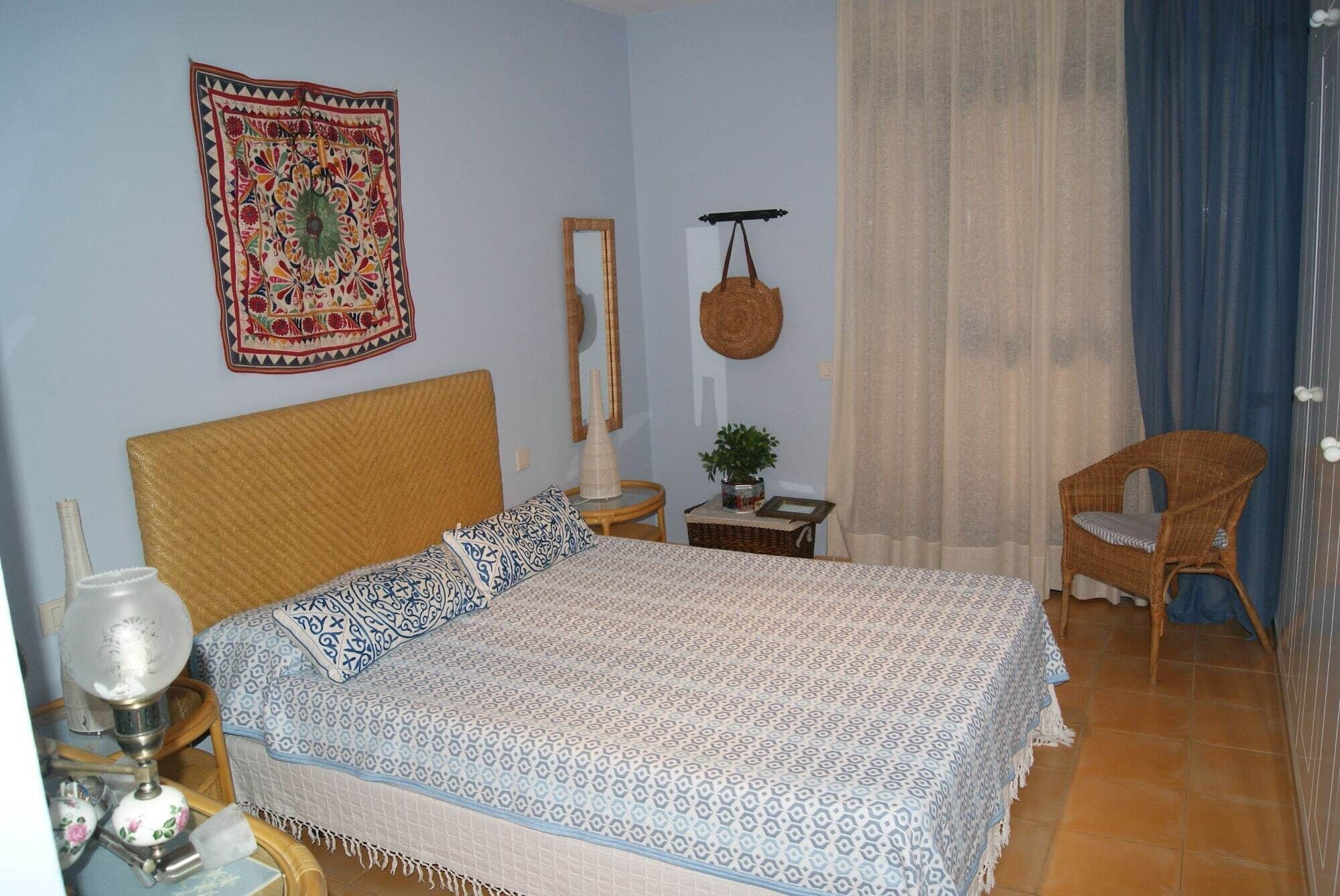 Ein Schlafzimmer mit einem Bett, einem Sessel, einem Nachttisch, einer Lampe, einer hängenden Ampel und einem Wandteppich.
