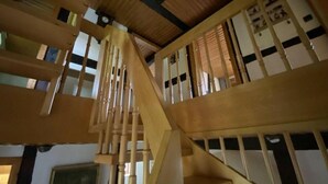 Una escalera de madera con barandilla, que sube a un piso superior con ventanas y un reloj.