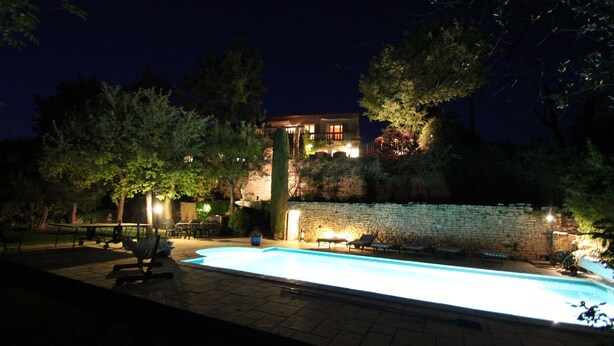 A nighttime view of a swimming pool area with lounge chairs and a stone wall. - Air-conditioned luxury farmhouse, heated pool,sport hall, billiard table soccer, (Robion)