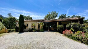 A two-story building with a tiled roof, a gravel driveway, and a garden with various plants and flowers. - Air-conditioned luxury farmhouse, heated pool,sport hall, billiard table soccer, (Robion)