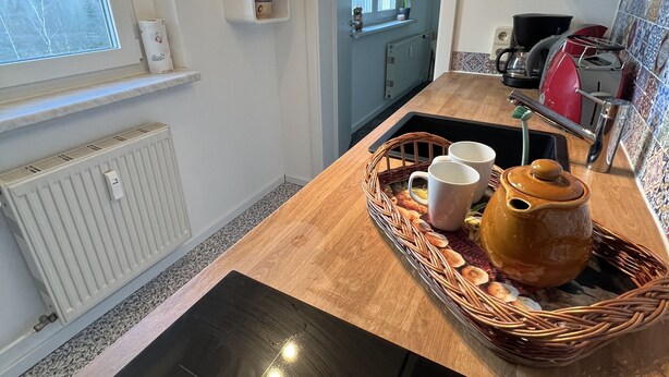 Een keuken met een houten aanrecht, een radiator, een raam en een deur die naar een andere kamer leidt.