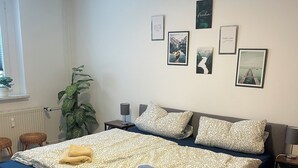 Een netjes opgemaakt bed met een bedsprei met dessin, een bedlampje en een wand met ingelijste foto's.