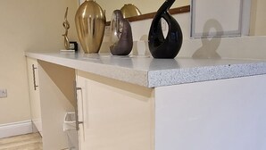 A modern kitchen with a white countertop, a large mirror, and a wooden floor. - Lily Pad by Paymán Club (Royston)