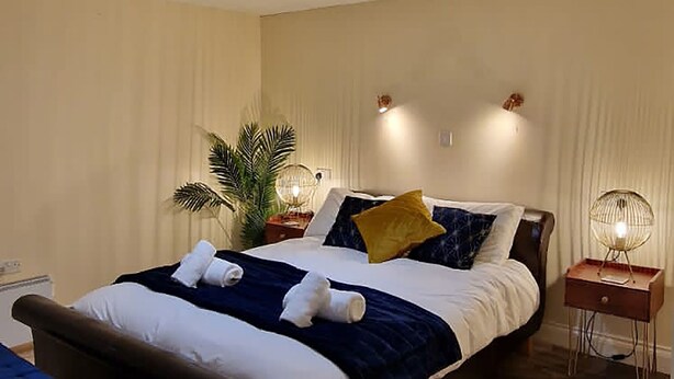 A neatly arranged bedroom with a large bed, bedside tables, a bedside lamp, and a potted plant. - Lily Pad by Paymán Club (Royston)