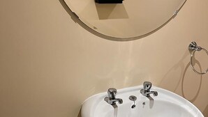 A bathroom with a white sink, two faucets, a mirror, a towel dispenser, and a toilet paper holder. - Lily Pad by Paymán Club (Royston)