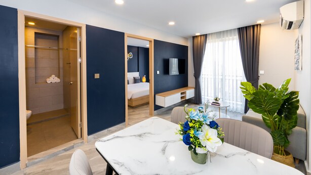 Quarto de hotel moderno com uma mesa de jantar de mármore, um sofá, uma planta grande e uma área de chuveiro.