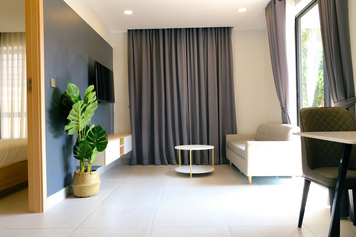 A modern living room with a sofa, a round coffee table, a potted plant, and a TV mounted on the wall.