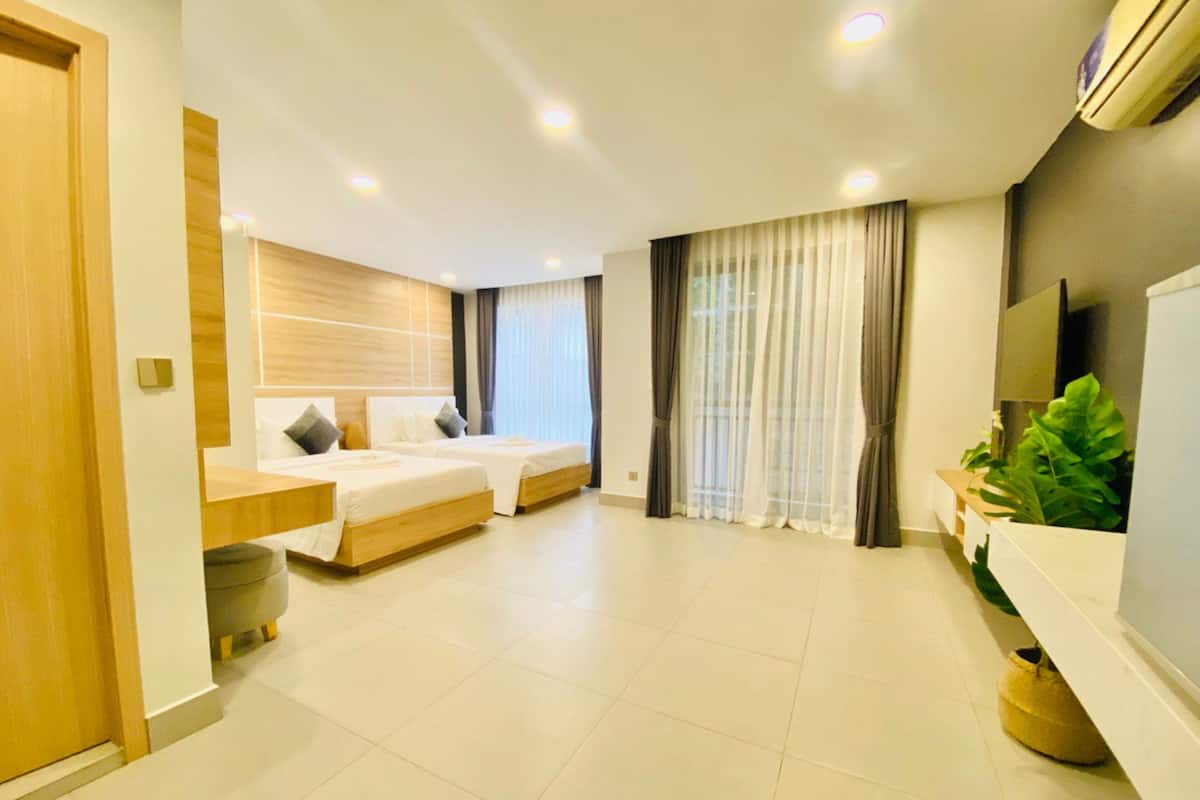 A modern hotel room with two beds, a large window with curtains, a flat-screen TV, and a potted plant.