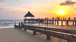 Uma praia com um píer que se estende até o oceano, com um coreto e pessoas caminhando.
