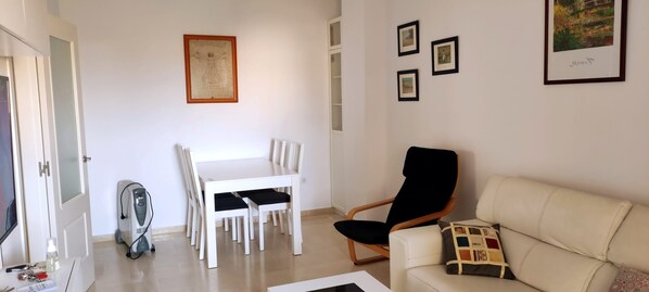 Un salon avec un canapé blanc, un fauteuil noir, une table à manger avec des chaises et un tableau encadré au mur.