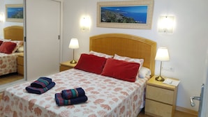 A neatly arranged hotel room with a bed, two bedside tables, a mirror, and a painting on the wall. - Horizon Apartment: Large Terrace and Panoramic Ocean View on the Waterfront (Los Cristianos)