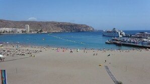 A beach with a large cruise ship docked, a rocky hill in the background, and a clear blue sky. - Horizon Apartment: Large Terrace and Panoramic Ocean View on the Waterfront (Los Cristianos)