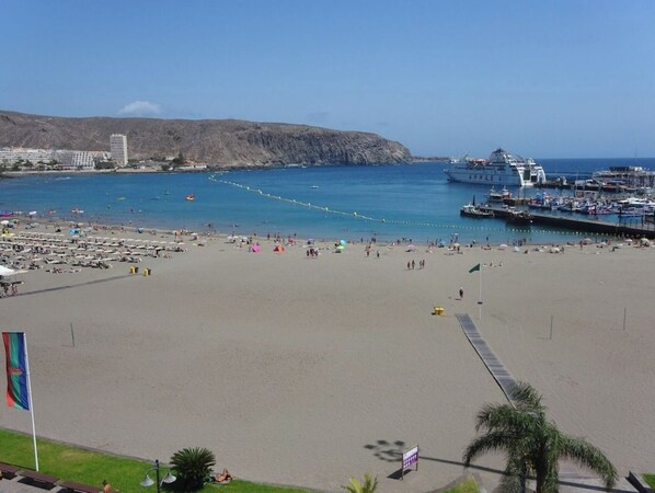 A beach with a large cruise ship docked, a rocky hill in the background, and a clear blue sky. - Horizon Apartment: Large Terrace and Panoramic Ocean View on the Waterfront (Los Cristianos)