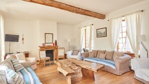 A spacious living room with a wooden coffee table, a sofa, and a couch. There is a fireplace, a television, and a window with curtains. - Le Presbytère, The Presbytery of Fourdrain (Fourdrain)
