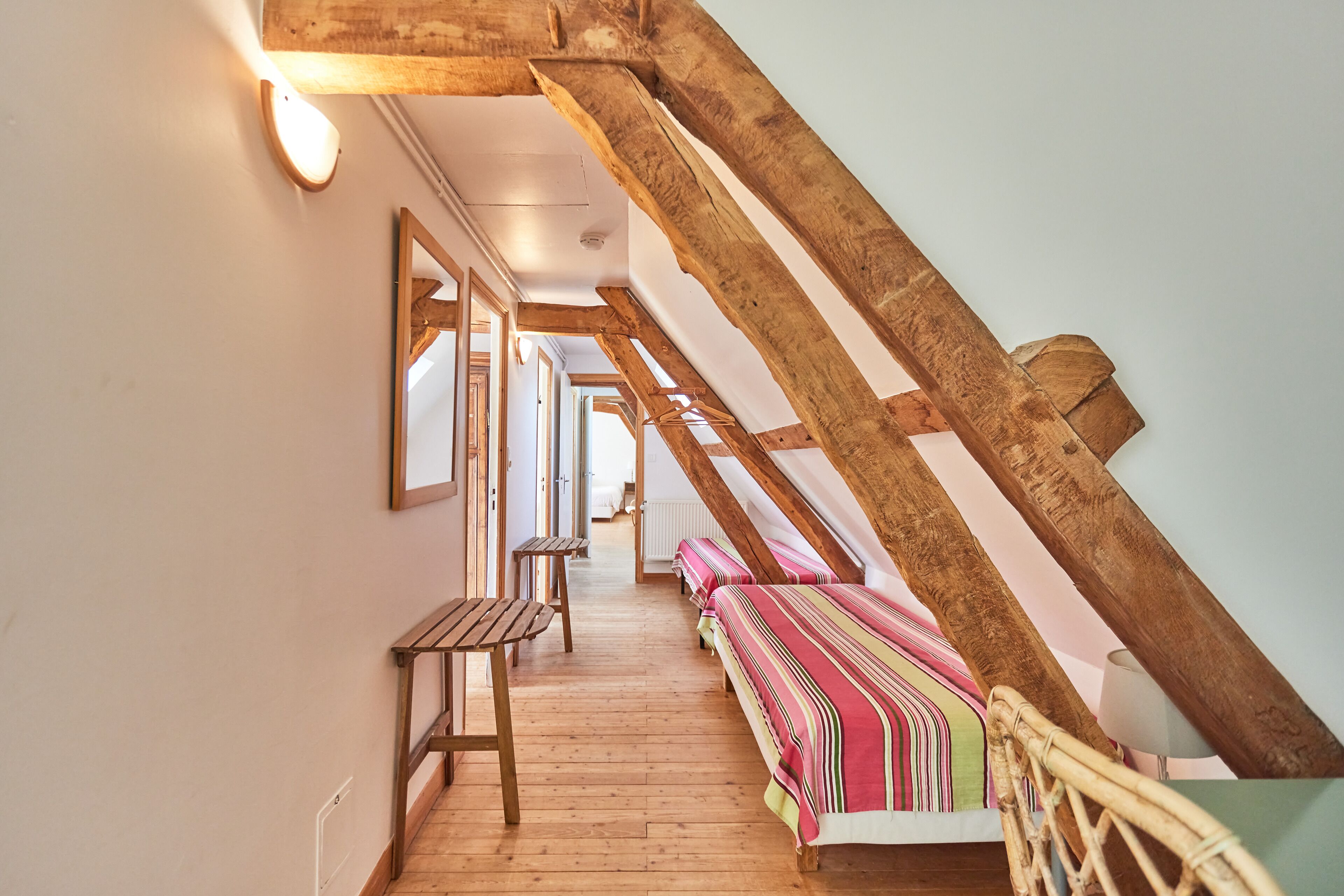 A narrow hallway with wooden beams, a bench, and a bed with striped bedding.