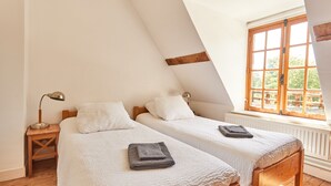A bedroom with two beds, wooden headboards, a window with a view, and a small bedside table with a lamp. - Le Presbytère, The Presbytery of Fourdrain (Fourdrain)
