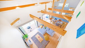 Un appartement spacieux de style « loft », avec des poutres apparentes, un coin repas comprenant une table et des chaises, un salon avec un canapé et une table basse, et une grande fenêtre laissant entrer la lumière naturelle.
