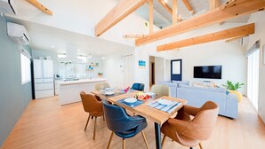 Une cuisine moderne avec des appareils électroménagers blancs, un coin repas avec des meubles en bois et un salon équipé d’un téléviseur et d’un canapé.