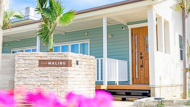 Un mur de pierre sur lequel est apposée une plaque indiquant « Villa Malibu », et une porte en bois.