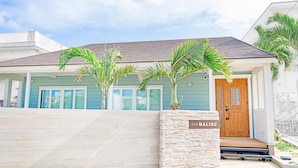Une villa avec une entrée surmontée d’un mur en pierre, une porte en bois et une enseigne indiquant « Villa Malibu ».