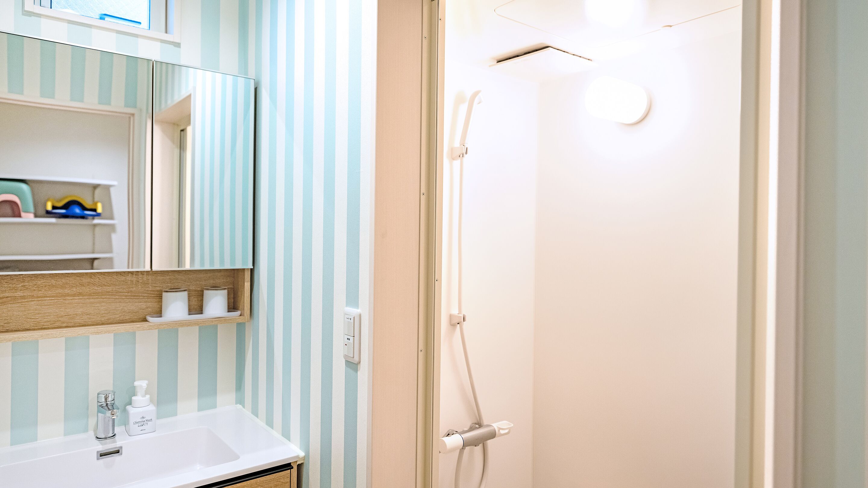 A bathroom with a striped wall, a mirror, a sink with toiletries, and a shower.