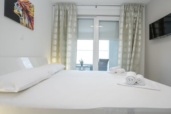 Une chambre d’hôtel avec un grand lit, des rideaux blancs, un téléviseur fixé au mur et une vue sur le balcon extérieur.