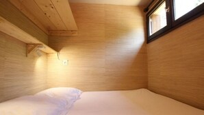Una habitación pequeña y acogedora con una cama individual, paredes de madera y una ventana.