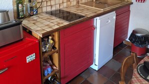Cocina compacta con un refrigerador rojo, microondas y lavavajillas. Paredes y salpicadero cubiertos de azulejos.