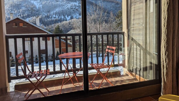 Un balcón con una mesa y sillas, con vistas a montañas nevadas y un edificio de madera al fondo.