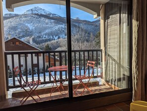 Ein Balkon mit Tisch und Stühlen, der Blick auf schneebedeckte Berge und ein Holzgebäude im Hintergrund bietet.