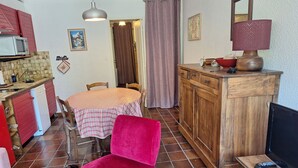 Cocina compacta con microondas, pileta y muebles de madera. Hay un comedor con mesa y sillas, y un televisor sobre un atril de madera.