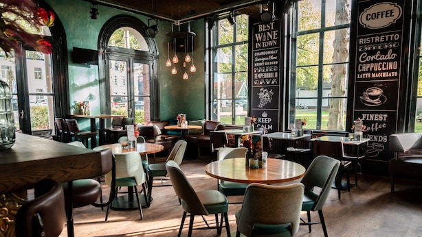 A cozy café interior with round tables, comfortable chairs, and large windows offering a view of the street. - Boutique Hotel Brasa Beemster (Middenbeemster)