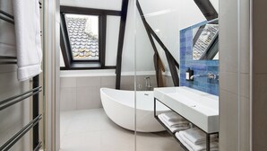 A modern bathroom with a freestanding bathtub, a glass shower enclosure, and a window with a view of the roof tiles. - Boutique Hotel Brasa Beemster (Middenbeemster)