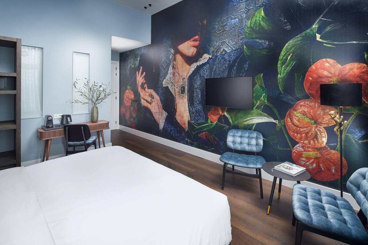 Een hotelkamer met een groot bed, een bureau met stoel, een kleine tafel met stoel, en een grote muurschildering.