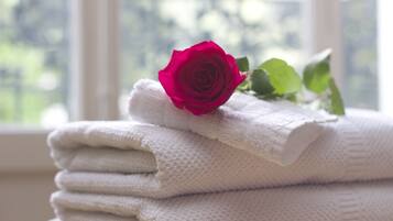 Una pila de toallas blancas con una rosa roja encima, colocada cerca de una ventana con vistas a la vegetación.