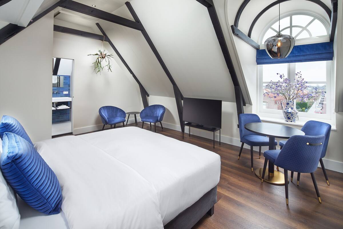 Een slaapkamer met een groot bed, een eettafel met stoelen, een televisie en uitzicht op de stad door een raam.