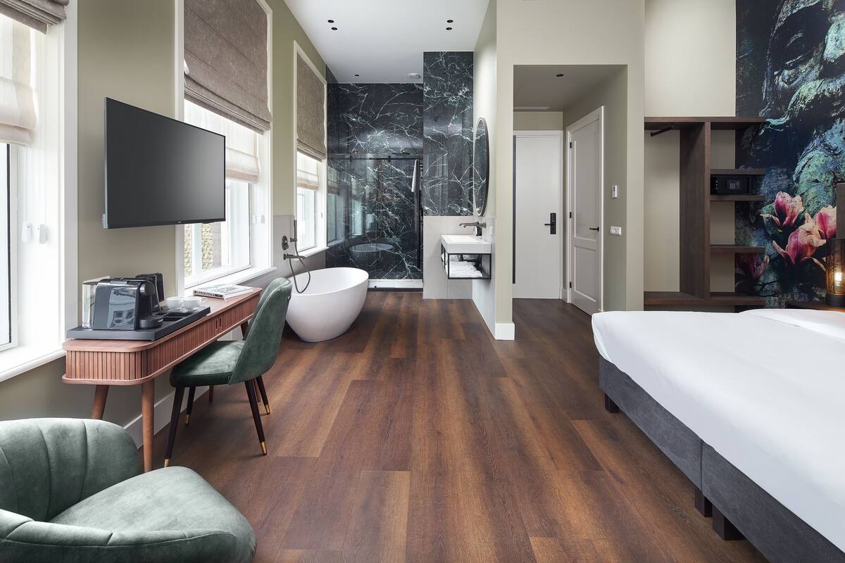 Een moderne hotelkamer met een groot bed, een bureau met computer, een stoel, een badkuip en een televisie.