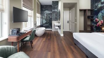 Una habitación de hotel moderna con una cama grande, un escritorio con computadora, una silla, una bañera y un televisor.