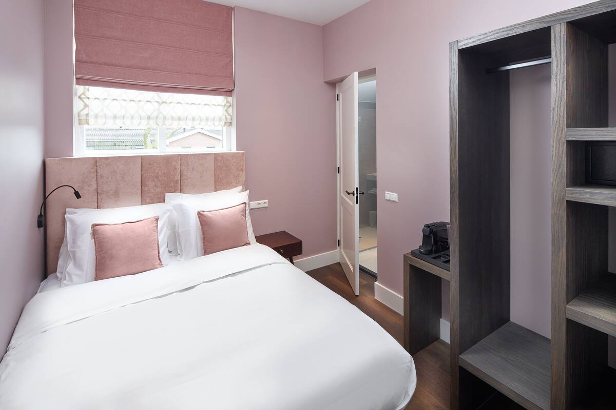 Een slaapkamer met een bed, nachtkastje, kledingkast en een raam met uitzicht.