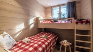 A bunk bed room with a checkered bedspread, a small table, and a ladder. - Chalet Les Carlines (Courchevel)