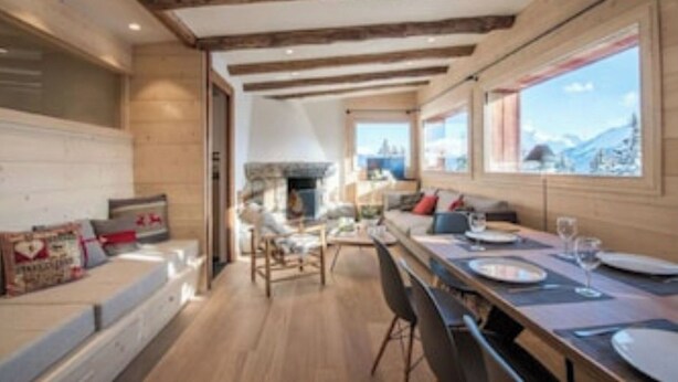 A modern kitchen with wooden beams, a dining area with a long table, and large windows offering a mountain view. - Chalet Les Carlines (Courchevel)