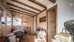 A room with exposed wooden beams, a dining area with a table and chairs, and a door leading to another room. - Chalet Les Carlines (Courchevel)