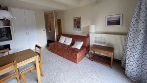 En kompakt opholdsstue med en rød sofa, et træbord, en hvid radiator og et mønstret gardin.