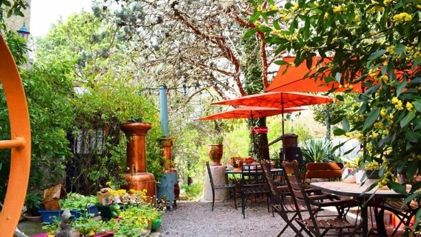 An outdoor patio area with a table and chairs, surrounded by potted plants and a gravel path.