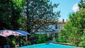 A swimming pool surrounded by lush greenery and a building with a tiled roof.