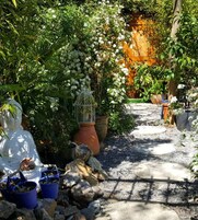Un sendero en un jardín con plantas en macetas y una estatua.